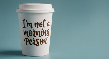Coffee cup with stylized brush script saying I'm not a morning person white lid on muted background cozy and humorous tone side angle