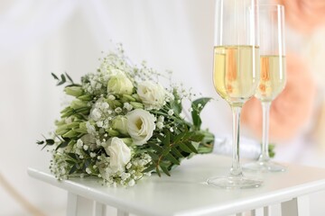 Glasses of champagne and wedding bouquet on table indoors, closeup