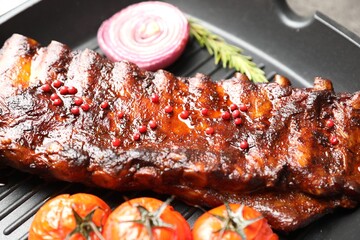Delicious roasted pork ribs with rosemary, onion and tomatoes on grill pan, closeup