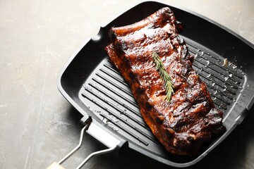 Delicious roasted pork ribs with rosemary on grey table, closeup