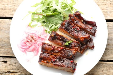 Delicious pork ribs, arugula and onion on wooden table, top view