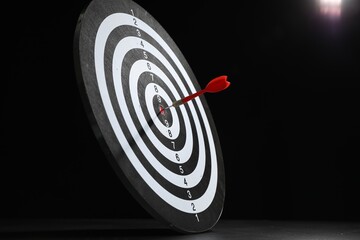 Targeting. Dart board with arrow on gray surface against black background
