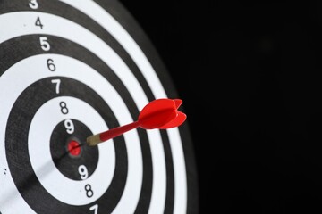 Targeting. Dart board with arrow on black background, closeup. Space for text
