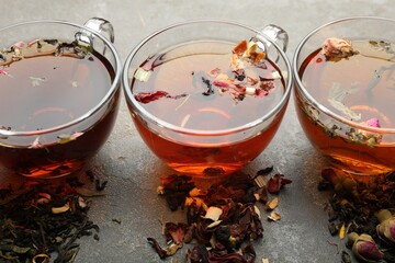 Aromatic herbal tea in glass cups and dry leaves on grey table, closeup