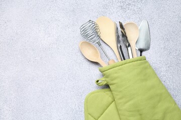 Different kitchen utensils in oven mitten on light table, top view. Space for text