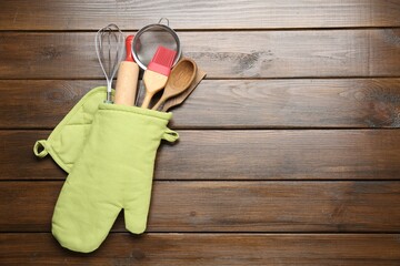 Different kitchen utensils in oven mitten on wooden table, top view. Space for text