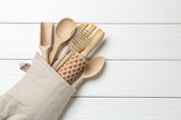 Different kitchen utensils in oven mitten on white wooden table, top view. Space for text