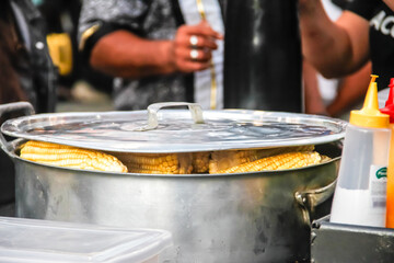 A large metal cooking pot filled with boiling liquid and corn is used during outdoor food preparation. The scene captures traditional large-scale cooking methods commonly used at festivals.