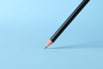 Sharp graphite pencil on light blue background, closeup. Space for text