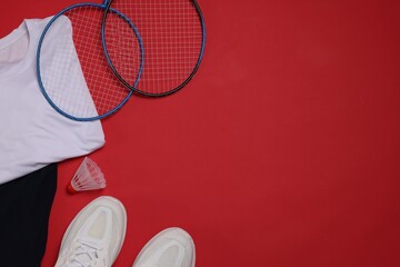 Sportswear, sneakers, badminton rackets and shuttlecock on red background, flat lay. Space for text