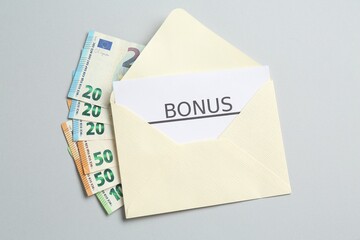 Envelope with money and word Bonus on light grey background, top view