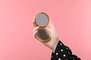 Woman holding open pocket mirror on pink background, closeup