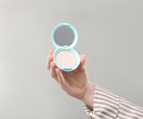 Woman holding open face powder with mirror on grey background, closeup