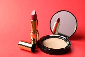 Open face powder with mirror and lipstick on red background, closeup
