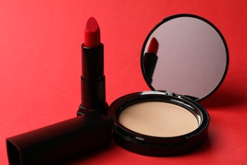 Open face powder with mirror and lipstick on red background, closeup