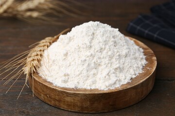 Wheat flour and spikes on wooden table, closeup