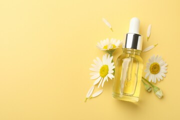 Bottle of essential oil and chamomile flowers on yellow background, flat lay. Space for text