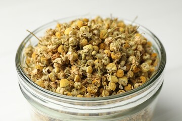 Dry chamomile flowers in glass jar on light table, closeup
