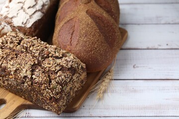 Fresh bread loaves and spikes on white wooden table, closeup