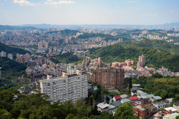 Fototapeta premium Panoramic view of a sprawling city with numerous buildings nestled among lush green hills under a clear sky, showcasing urban development and natural landscape.
