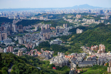 Fototapeta premium Panoramic aerial view of a sprawling city nestled among lush green hills and mountains under a clear sky, urban landscape.