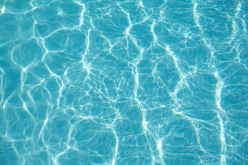 Bright blue swimming pool water with shimmering sunlight reflections, Summer background.