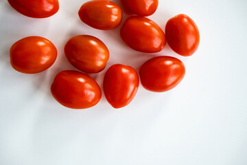 Top view of ripe red cherry tomatoes arranged on a white surface. The vibrant color of the tomatoes contrasts with the plain background, highlighting their freshness and natural appeal.