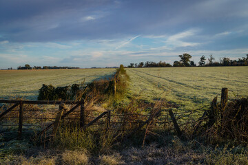 Winter landscape of a field with frost, a fence and blue sky