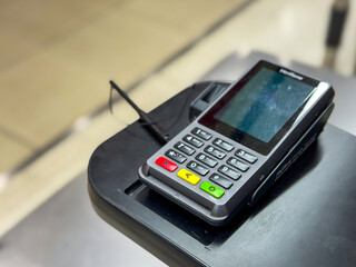Close-up shot of a modern payment terminal placed on a retail counter. The card reader features a numeric keypad