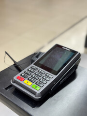 Close-up shot of a modern payment terminal placed on a retail counter. The card reader features a numeric keypad