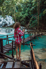 Traveller woman take pictures on phone on bridge at cascade waterfall in Luwuk, Sulawesi, Indonesia