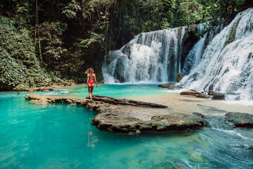 Woman in swimsuit on rock at scenic cascade waterfalls with turquoise water