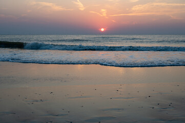 Sunset over the sea, with waves and sandy beach