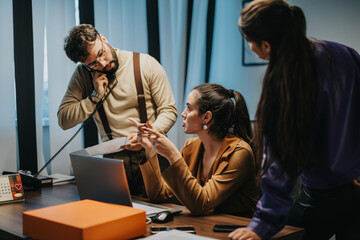 Three colleagues engage in an office discussion, exchanging ideas and using resources to...