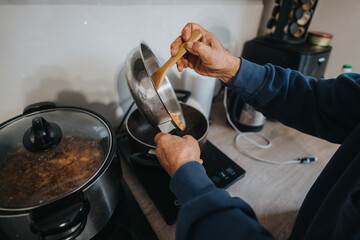 A person prepares a meal in a modern home kitchen, stirring ingredients on a stove top, showcasing culinary practices and cozy domestic life.