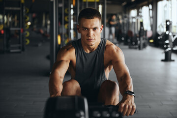 Concentrated attractive man working out on rowing device in contemporary gym. Active young fellow...