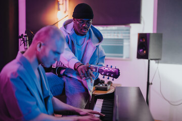 Two diverse musicians work together in a professional studio setting. One plays the guitar while the other focuses on a keyboard, creating an inspiring and dynamic atmosphere for music production.