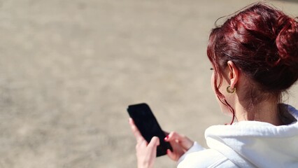 girl using smartphone writing message scrolling news feed watching content. girl sitting on bench...