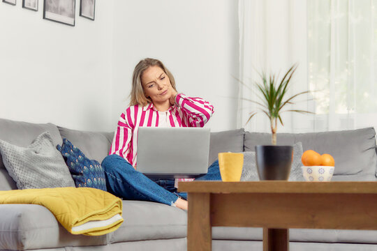 Businesswoman suffering from neck pain while working on laptop at home office. Tech neck or computer syndrome. Young female under pressure