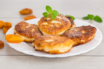 Fresh cottage cheese pancakes with pieces of dried apricots and a leaf of mint
