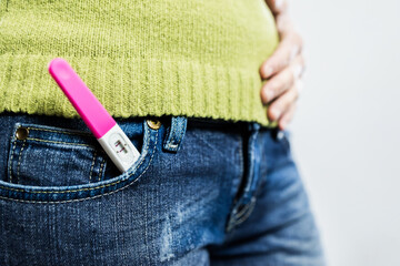 Positive pregnancy test tucked into jeans pocket with hand on belly. Lifestyle.