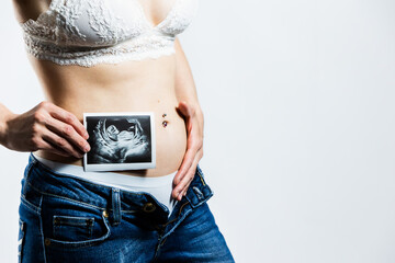 Pregnant woman showing ultrasound image near belly. Lifestyle.