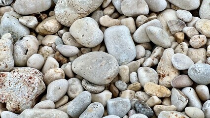 Smooth sea pebbles cover the shore in a natural coastal pattern. Beach texture, marine background, nature detail, seaside calm, minimalist composition, ocean shore, relaxation, travel mood. 