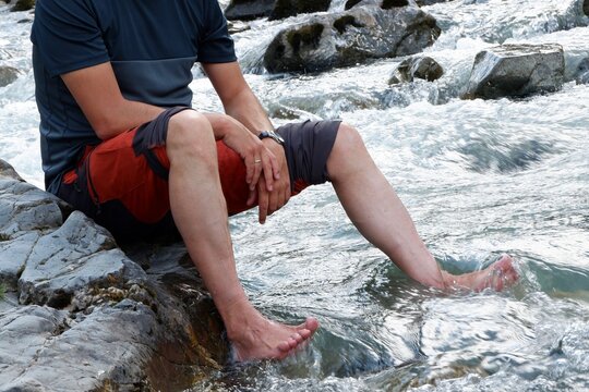 A person sits on a rocky riverbank, dipping their feet into the cool water while enjoying the peaceful atmosphere of nature