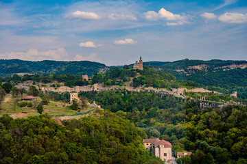 Fototapeta premium Wide View of Tsarevets Fortress Surrounded by Forested Hills and Ancient Walls in Veliko Tarnovo, Bulgaria under a Partly Cloudy Sky
