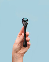 Woman holding black facial derma roller on blue background with copy space