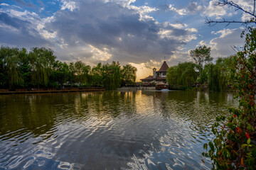 Obraz premium Tranquil Lakeside Scene at Sunset with Reflections, Weeping Willows, and Rustic Architecture in Gorna Malina, Near Sofia, Bulgaria