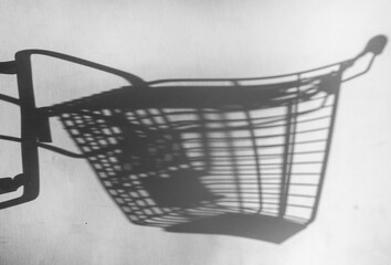 Shadow of a supermarket shopping cart on a white background with sunlight. Minimalist shopping concept.