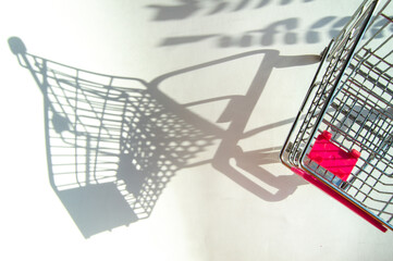 Shadow of a supermarket shopping cart on a white background with sunlight. Minimalist shopping concept.