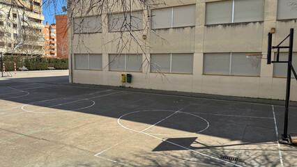 Quiet urban basketball court basking in midday sun, echoes of streetball dreams, perfect for...